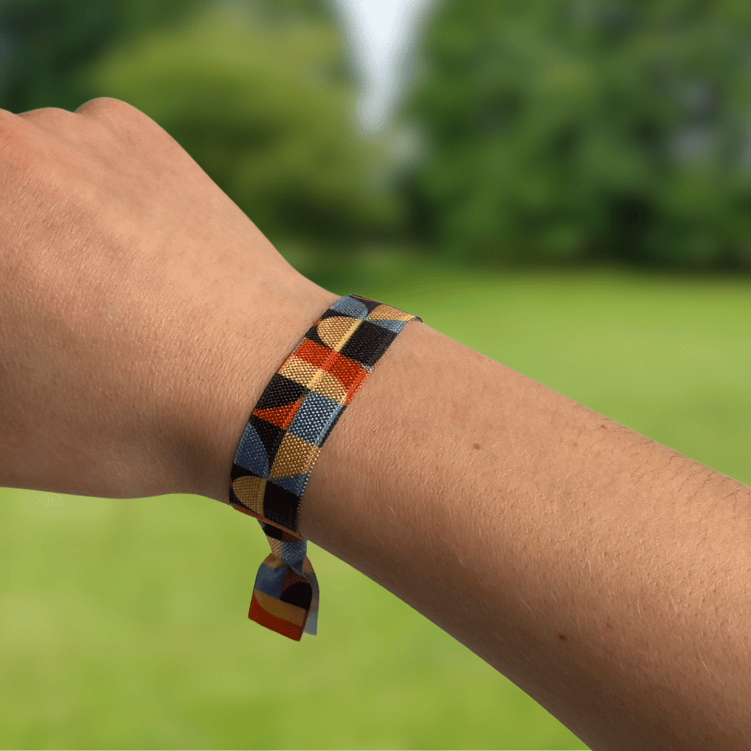 70er Jahre Muster Hairtie Armband Haargummi an einem Arm. Im Hintergrund ist ein Hundepark