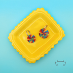Zwei personalisierte runde Acryl-Hundemarken mit buntem Groovy-Lollipop-Design auf einem gelben Tablett vor türkisfarbenem Hintergrund.