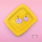 Zwei runde Acryl-Hundemarken im rosa Y2K-Design mit spiralförmigem Muster, Name und Telefonnummer, auf einem gelben Tablett vor rosa Hintergrund.