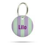 Personalisierte runde Acryl-Hundemarke für Hunde mit pastellgrünem und fliederfarbenem Streifenmuster, lila Name „Lilo“ und silbernem Schlüsselring auf weißem Hintergrund.