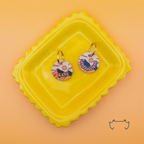 Zwei runde personalisierte Acryl-Hundemarken mit beige-orangem Sonnenuntergangs- und Bergmotiv auf einem gelben Tablett vor warmem orangefarbenem Hintergrund.