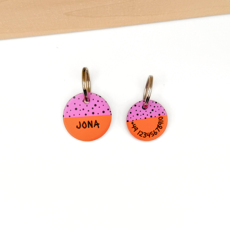 auf einem weißen Boden liegen zwei knallig bunte personalisierte Hundemarken aus Acryl in orange und rosa, ähnlich einer Drachenfrucht. Sie sind leicht und geräuschlos
