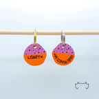 Zwei personalisierte runde Acryl-Hundemarken im pink-orangenen Drachenfrucht-Design an einer hellen Stange, vorne mit Name „Lisbeth“ und hinten mit Telefonnummer.