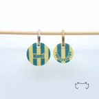 Zwei personalisierte runde Acryl-Hundemarken im petrol-beige gestreiften Design an einer hellen Holzstange, vorne mit Name „Nami“ und hinten mit Telefonnummer.