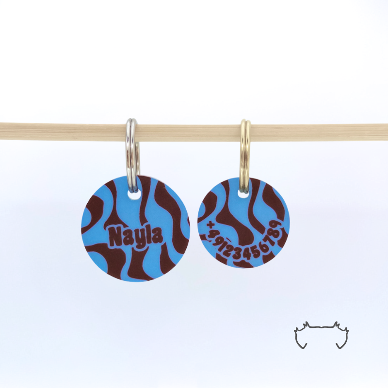 Zwei runde personalisierte Acryl-Hundemarken mit blauem und bordeauxfarbenem Wellen-Design an einer hellen Holzstange, vorne mit Name und hinten mit Telefonnummer.