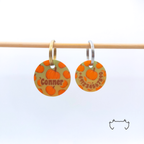 Zwei runde Acryl-Hundemarken im orangefarbenen Halloween-Kürbis-Design an einer hellen Holzstange, vorne mit Name und hinten mit Telefonnummer.