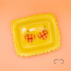 Zwei formgeschnittene, bunte Acryl-Hundemarken in Herzform auf einem gelben Tablett vor apricotfarbenem Hintergrund. Die leichten Hundemarken haben ein orange-gelbes Streifenmuster und sind mit Name und Telefonnummer personalisiert.