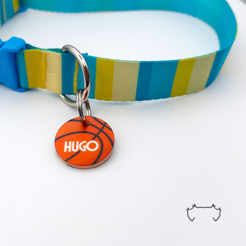 Runde Acryl-Hundemarke im Basketball-Design mit personalisiertem Namen, befestigt an einem türkis-gelb gestreiften Hundehalsband mit blauem Verschluss.