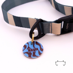 Personalisierte runde Acryl-Hundemarke mit blau-bordeauxfarbenem Wellenmuster und Name, befestigt an einem dunkelgrün-beige gestreiften Hundehalsband mit schwarzem Verschluss.