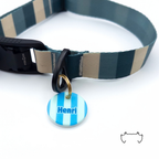 Personalisierte runde Hundemarke aus Acryl mit hellblauem und türkisem Streifenmuster und Name „Henri“, befestigt an einem dunkelgrün-beige gestreiften Hundehalsband mit schwarzem Verschluss.