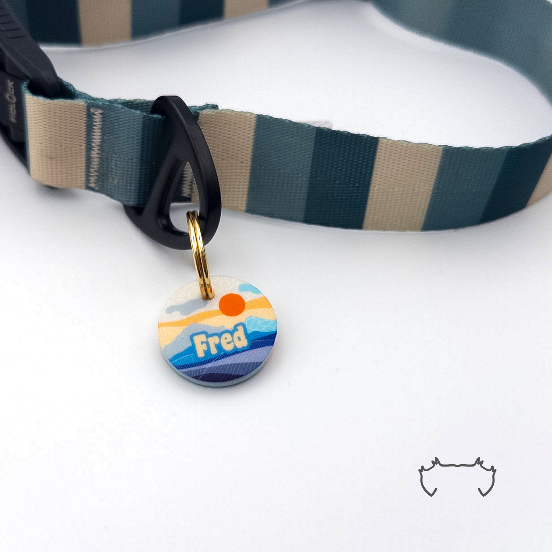 Runde personalisierte Acryl-Hundemarke mit blau-orangem Sunrise-Bergmotiv, befestigt an einem dunkelgrün-beige gestreiften Hundehalsband mit schwarzem Verschluss.