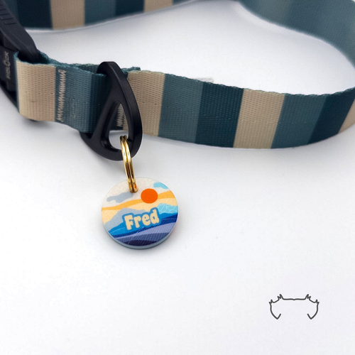 Runde personalisierte Acryl-Hundemarke mit blau-orangem Sunrise-Bergmotiv, befestigt an einem dunkelgrün-beige gestreiften Hundehalsband mit schwarzem Verschluss.