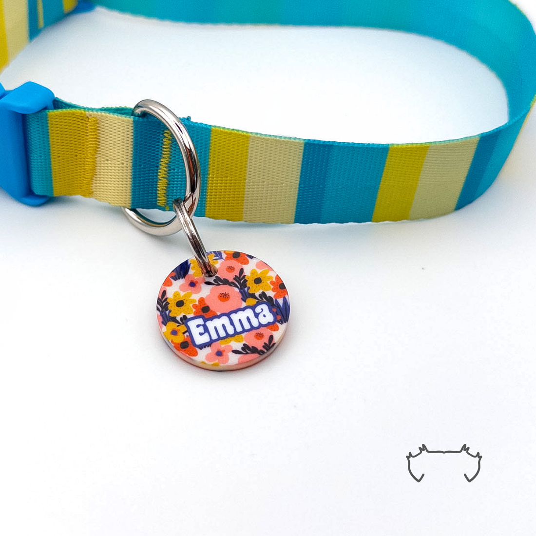 Runde personalisierte Hundemarke aus Acryl mit buntem Blumenmuster in Orange, Rot, Blau und Gelb, befestigt an einem türkis-gelb gestreiften Hundehalsband.