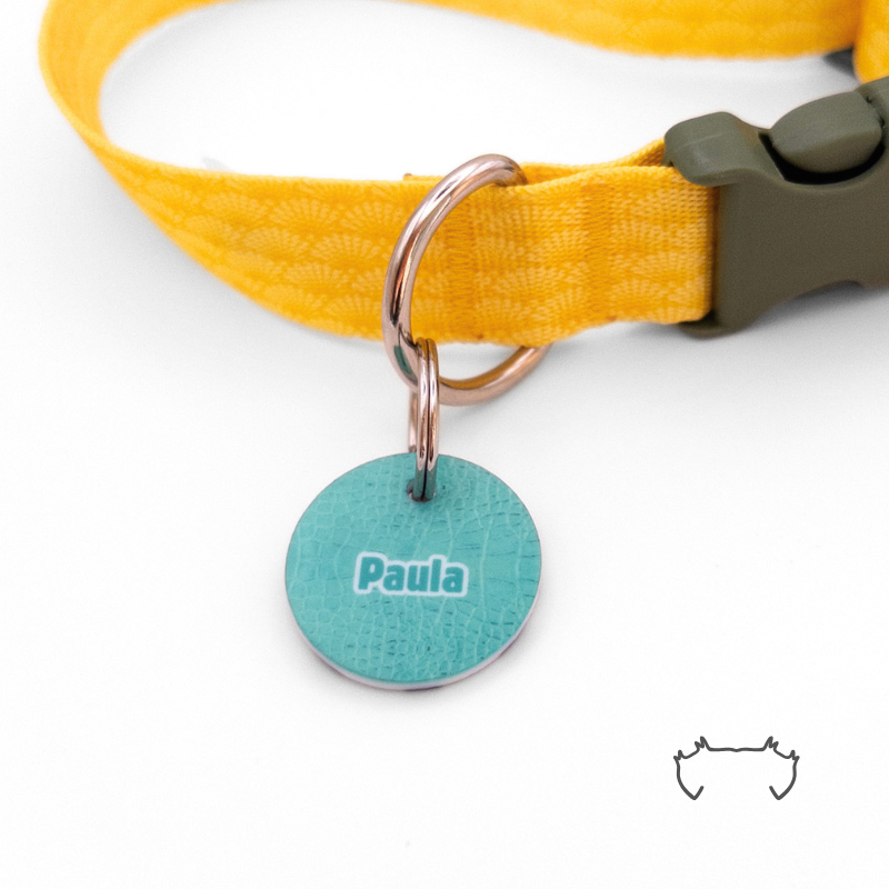 Runde personalisierte Acryl-Hundemarke im türkisfarbenen Croco-Animal-Print mit Name „Paula“, befestigt an einem gelben Hundehalsband mit schwarzem Verschluss.