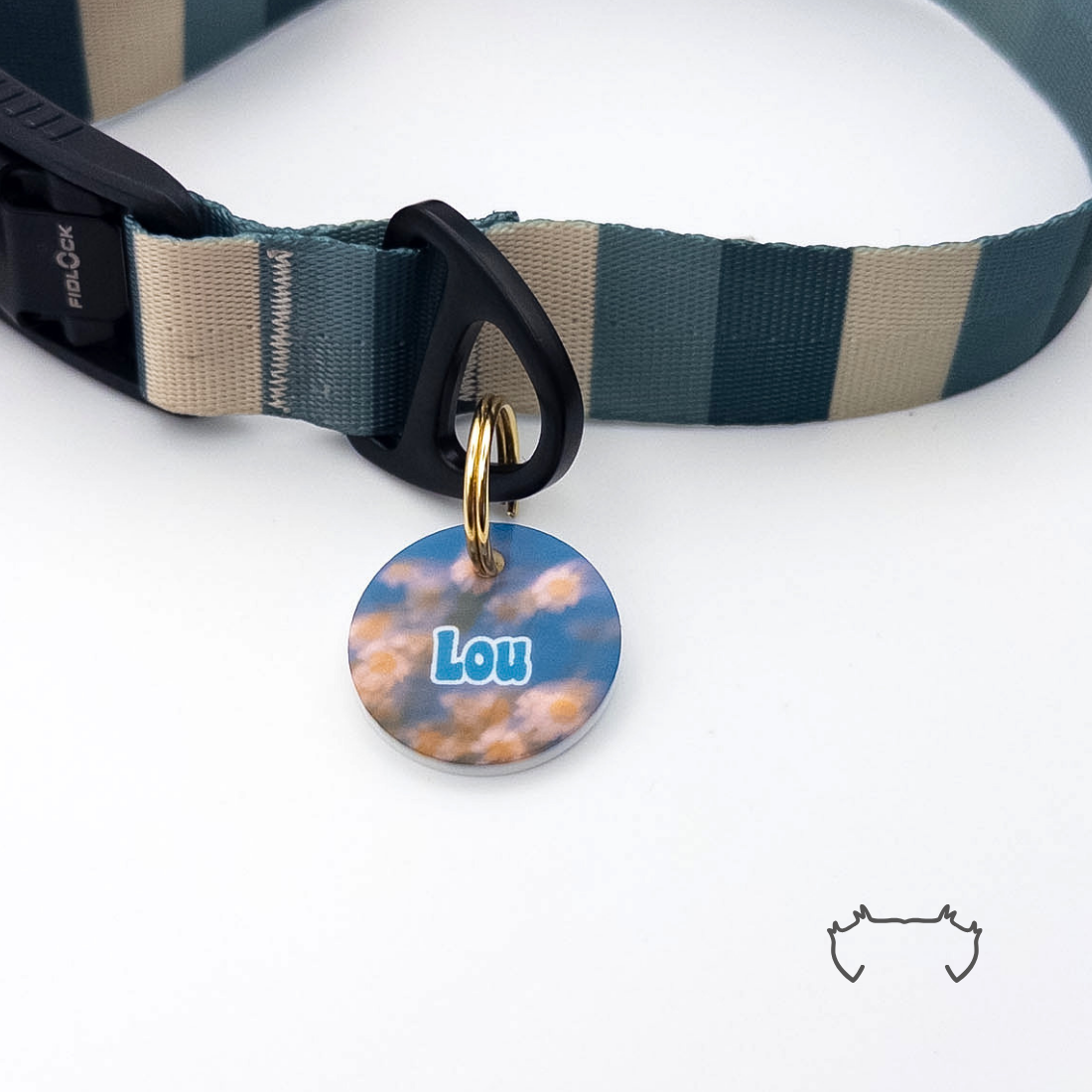 Runde personalisierte Acryl-Hundemarke mit blauem Gänseblümchen-Design und Name, befestigt an einem dunkelgrün-beige gestreiften Hundehalsband mit schwarzem Verschluss.