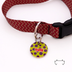 Runde personalisierte Acryl-Hundemarke mit grünem Hintergrund, lila Punkten und Name „Tony“, befestigt an einem bordeauxroten Hundehalsband mit Chevron-Muster und schwarzem Verschluss.
