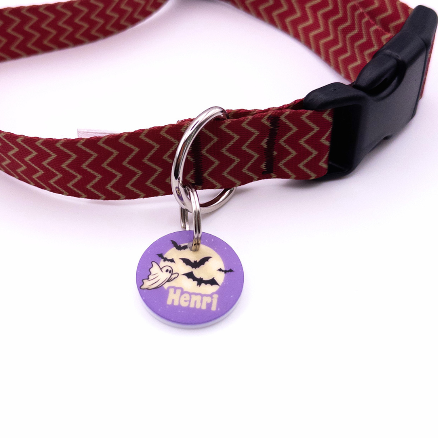 Runde personalisierte Acryl-Hundemarke im lila Halloween-Design mit Geist- und Mondmotiv, befestigt an einem bordeauxroten Hundehalsband mit schwarzem Verschluss.
