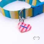 Formgeschnittene Acryl-Hundemarke in Herzform mit pinkem Streifenmuster, befestigt an einem türkis-gelb-beigen Hundehalsband mit blauem Verschluss. Bunte leichte personalisierte Hundemarke für Hunde.