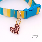 Personalisierte Acryl-Hundemarke in Herzform mit braunem Leo-Print, befestigt an einem türkis-gelb-beigen Hundehalsband mit blauem Verschluss. Die leichte, bunte Hundemarke ist mit dem Namen „Zula“ personalisiert.
