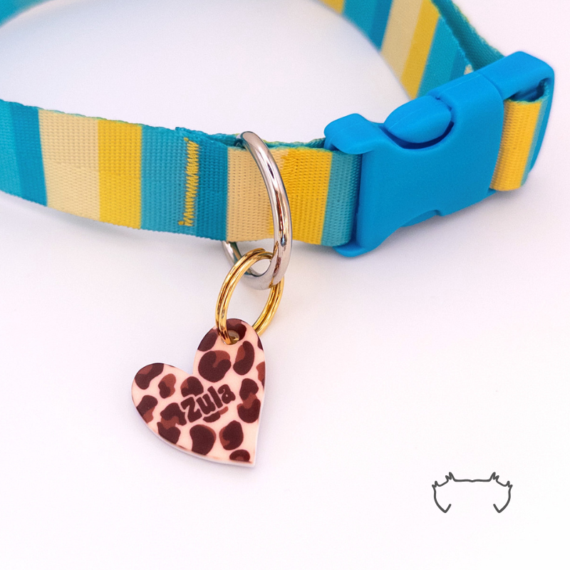 Personalisierte Acryl-Hundemarke in Herzform mit braunem Leo-Print, befestigt an einem türkis-gelb-beigen Hundehalsband mit blauem Verschluss. Die leichte, bunte Hundemarke ist mit dem Namen „Zula“ personalisiert.