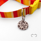 Runde personalisierte Acryl-Hundemarke im beige-braunen Leopard-Design, befestigt an einem rot-gelb gestreiften Hundehalsband mit gelbem Verschluss.