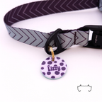 Personalisierte runde Acryl-Hundemarke mit lila Punkte-Design und Name „Lizzy“, befestigt an einem grauen Hundehalsband mit dunklem Chevron-Muster und schwarzem Verschluss.