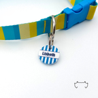 Runde personalisierte Acryl-Hundemarke im blau-weiß gestreiften Matrosen-Design, befestigt an einem türkis-gelb-beige gestreiften Hundehalsband mit blauem Verschluss.