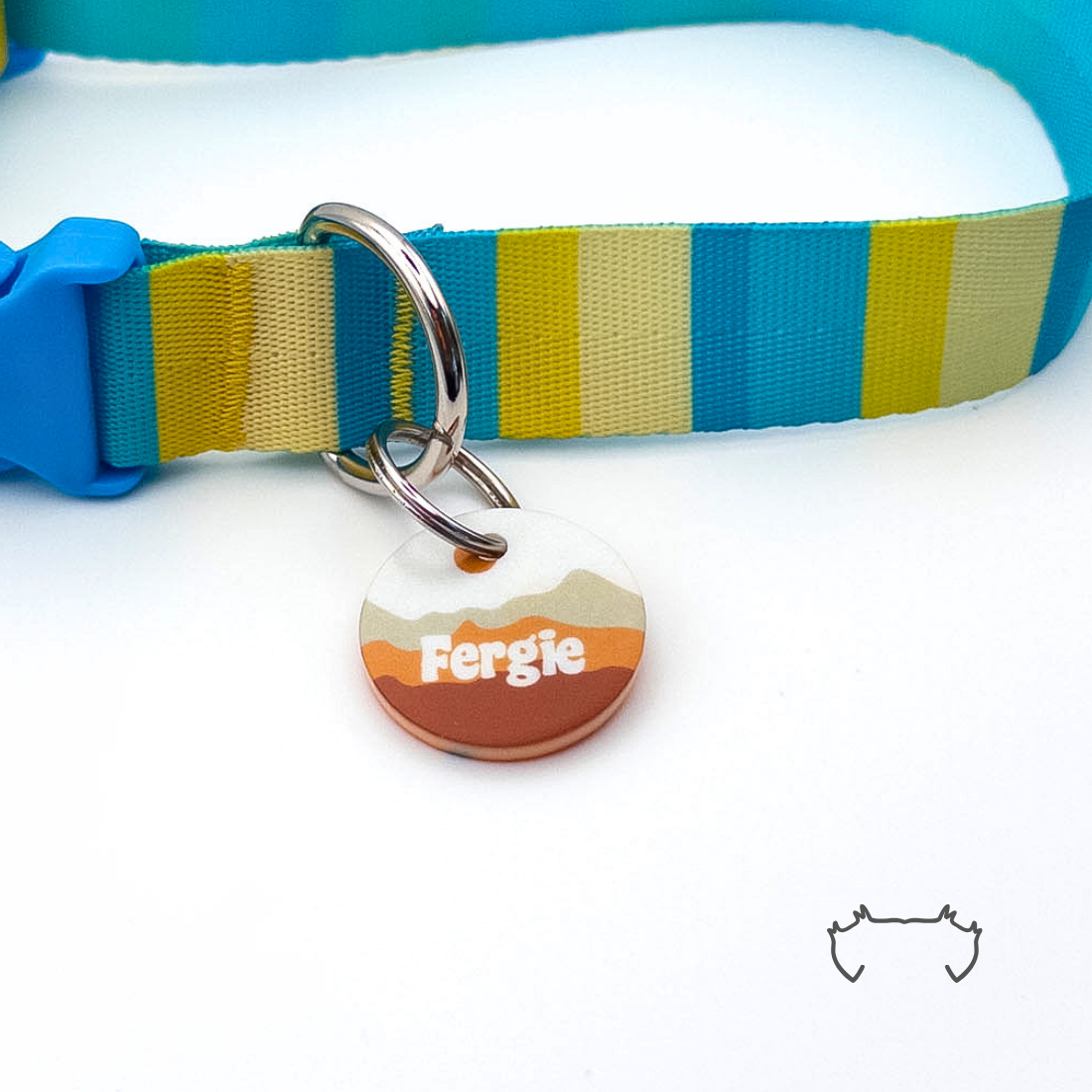 Runde personalisierte Acryl-Hundemarke mit braunem Bergmotiv und Name, befestigt an einem türkis-gelb-beige gestreiften Hundehalsband mit blauem Verschluss.