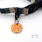 Personalisierte runde Acryl-Hundemarke mit orange-lila Punkte-Design und Name „Murphy“, befestigt an einem dunkelgrün-beige gestreiften Hundehalsband mit schwarzem Verschluss.