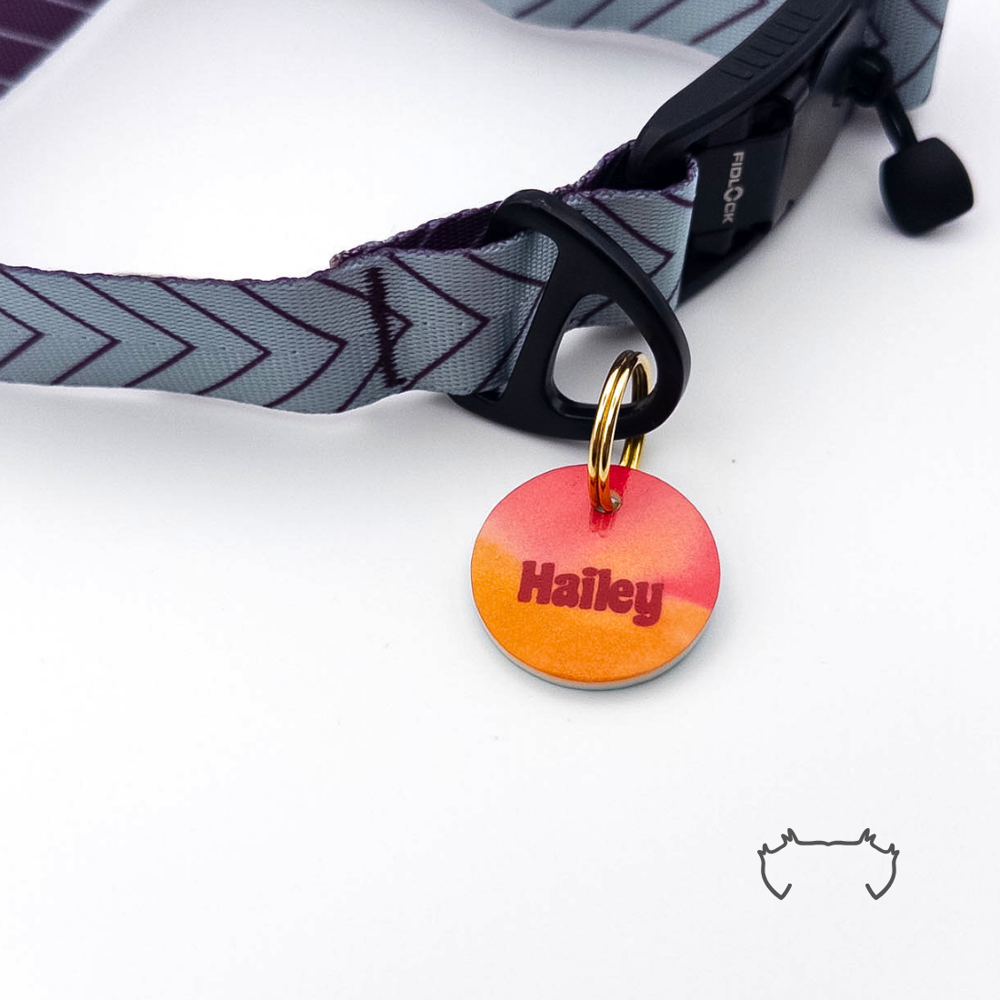 Runde personalisierte Acryl-Hundemarke mit Orange-Pink-Gradient, befestigt an einem grauen Hundehalsband mit dunklem Chevron-Muster und schwarzem Verschluss.