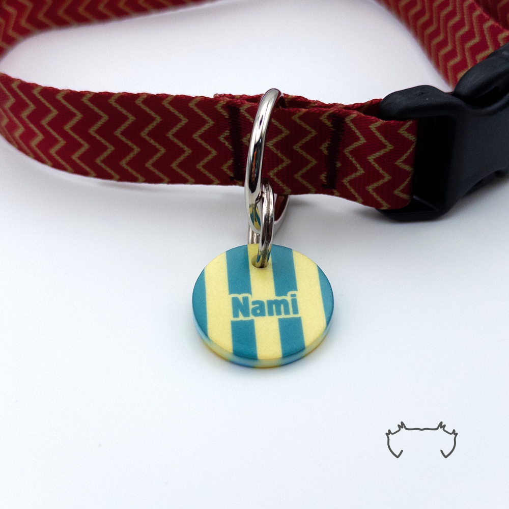 Runde personalisierte Acryl-Hundemarke mit petrol-beigem Streifenmuster und Name „Nami“, befestigt an einem bordeauxroten Hundehalsband mit goldfarbenem Chevron-Muster und schwarzem Verschluss.