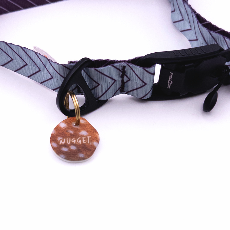 Personalisierte runde Acryl-Hundemarke im braunen Reh- und Bambi-Animalprint, befestigt an einem grauen Hundehalsband mit dunklem Chevron-Muster und schwarzem Verschluss.