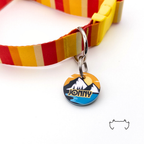 Personalisierte runde Acryl-Hundemarke im gelb-blauen Roadtrip-Design mit Bergmotiv, befestigt an einem rot-gelb gestreiften Hundehalsband mit gelbem Verschluss.