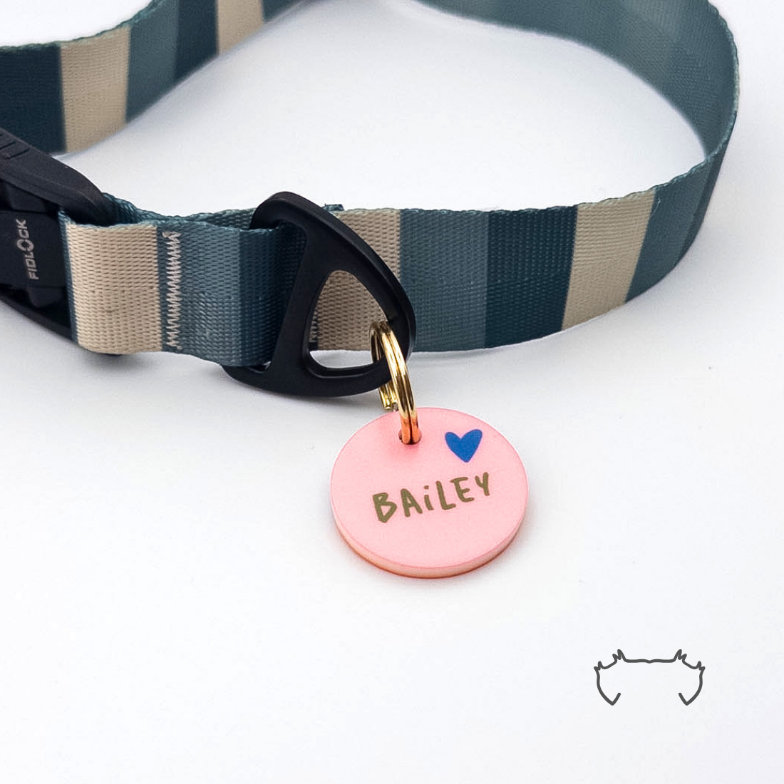 Runde personalisierte Acryl-Hundemarke in zartem Rosa mit Herzmotiv und Name, befestigt an einem dunkelgrün-beige gestreiften Hundehalsband mit schwarzem Verschluss.