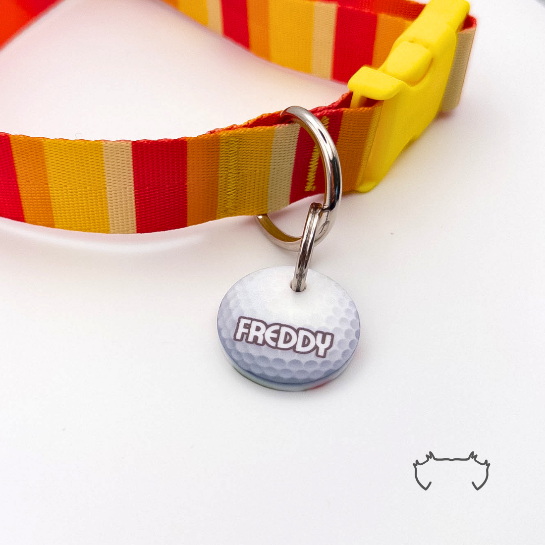 Runde Acryl-Hundemarke im weißen Golfball-Design mit personalisiertem Namen, befestigt an einem rot-gelb gestreiften Hundehalsband mit gelbem Verschluss.