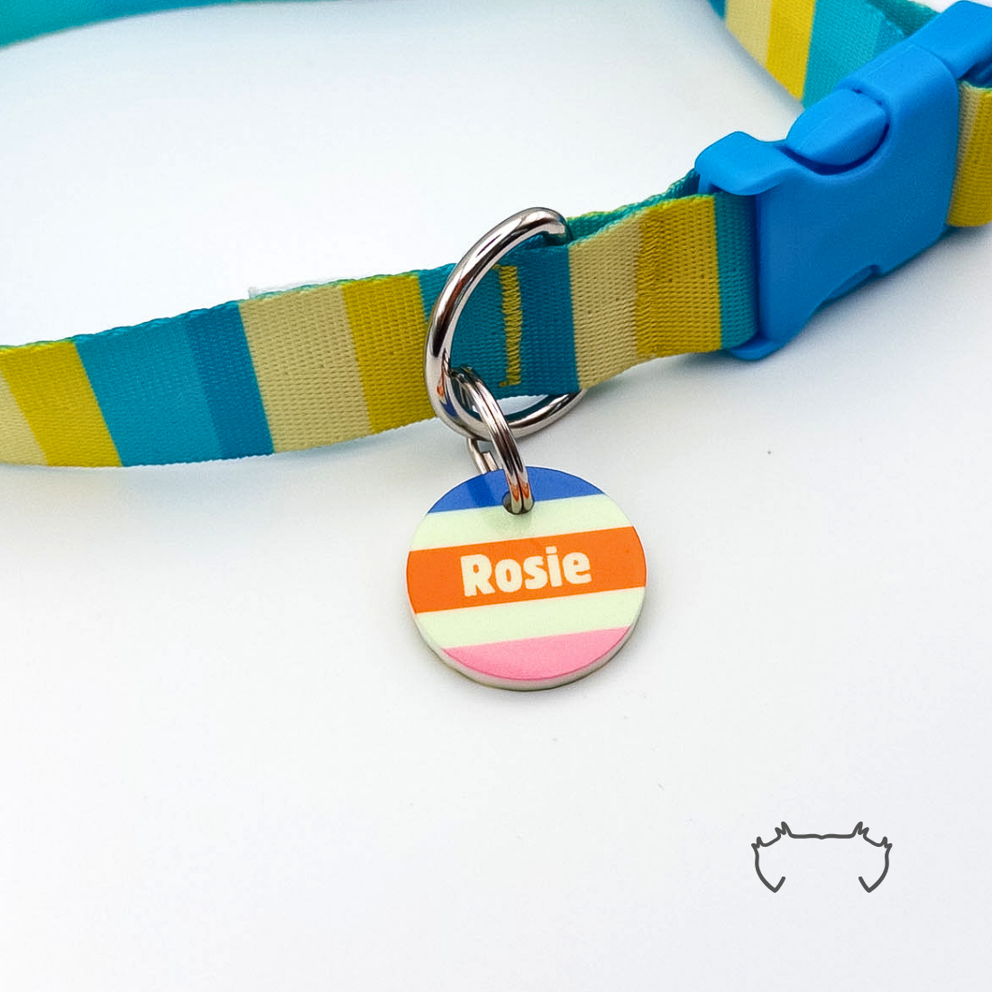 Personalisierte runde Acryl-Hundemarke mit mehrfarbigem Streifenmuster in Blau, Orange, Rosa und Creme, befestigt an einem türkis-gelb gestreiften Hundehalsband mit blauem Verschluss.