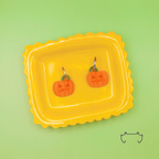 Zwei leichte, formgeschnittene Acryl-Hundemarken in Kürbisform auf einem gelben Tablett vor hellgrünem Hintergrund. Die bunten Hundemarken zeigen ein orangefarbenes Halloween-Kürbis-Design mit Personalisierung.