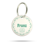 Runde personalisierte Wiesn Hundemarke aus Acryl mit grünen Ornamenten, Brezelmotiv, Name Franz und silberfarbenem Metallring.