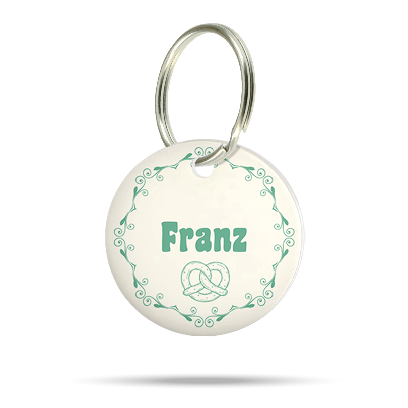 Runde personalisierte Wiesn Hundemarke aus Acryl mit grünen Ornamenten, Brezelmotiv, Name Franz und silberfarbenem Metallring.