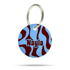 Personalisierte runde Hundemarke aus Acryl mit blauem und bordeauxrotem Wellenmuster, Name „Nayla“ und silbernem Schlüsselring auf weißem Hintergrund.