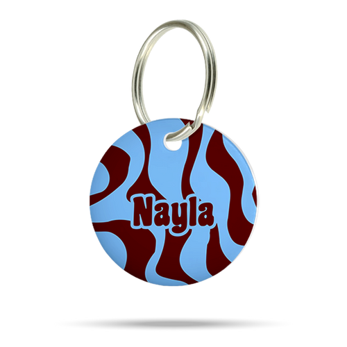 Personalisierte runde Hundemarke aus Acryl mit blauem und bordeauxrotem Wellenmuster, Name „Nayla“ und silbernem Schlüsselring auf weißem Hintergrund.