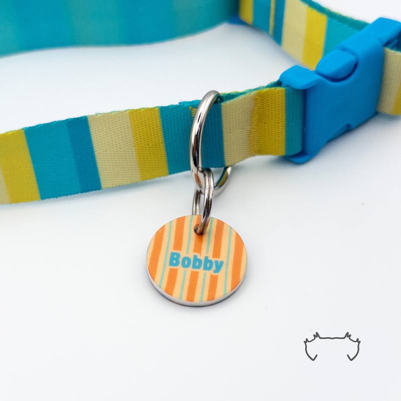 Runde personalisierte Hundemarke aus Acryl mit buntem Streifenmuster in Orange, Gelb, Creme und Türkis, befestigt an einem passenden gestreiften Hundehalsband mit blauem Kunststoffverschluss.