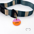 Runde personalisierte Acryl-Hundemarke mit neonorangefarbenem Untergrund, lila Muster und Name, befestigt an einem dunkelgrün-beige gestreiften Hundehalsband.