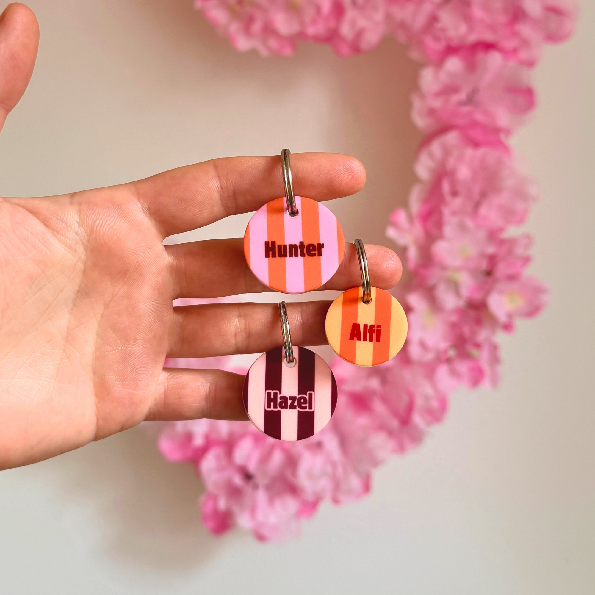 Hand hält zwei gestreifte personalisierte Hundemarken aus Acryl in orange und rosa, leicht und geräuschlos
